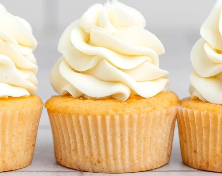 Freshly baked vanilla cupcakes with creamy frosting on a wooden table