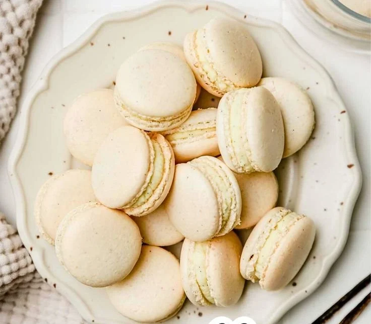 A plate of beautifully arranged vanilla macarons, showcasing their cream-filled centers.