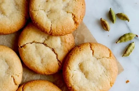 Freshly baked cardamom cookies on a wooden plate topped with cardamom pods.