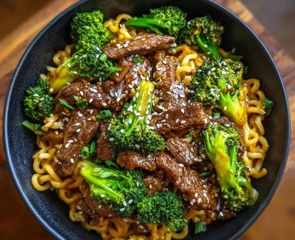 Plate of Chinese crispy beef with broccoli and noodles garnished with sesame seeds.