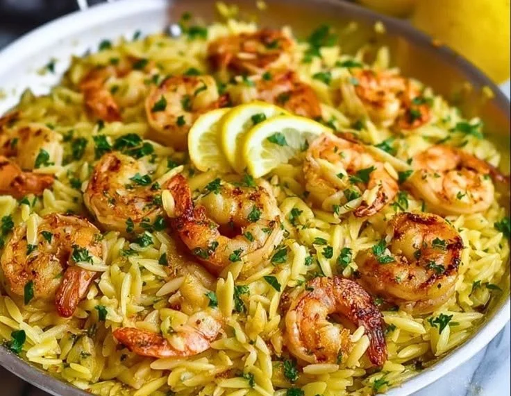 Lemon garlic shrimp served over orzo pasta with lemon slices and garnished with parsley.