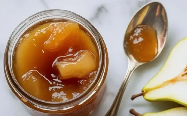 Homemade pear jam in a glass jar with fresh pears on a wooden table.