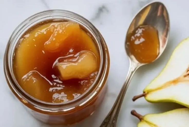 Homemade pear jam in a jar with fresh pears and a spoon