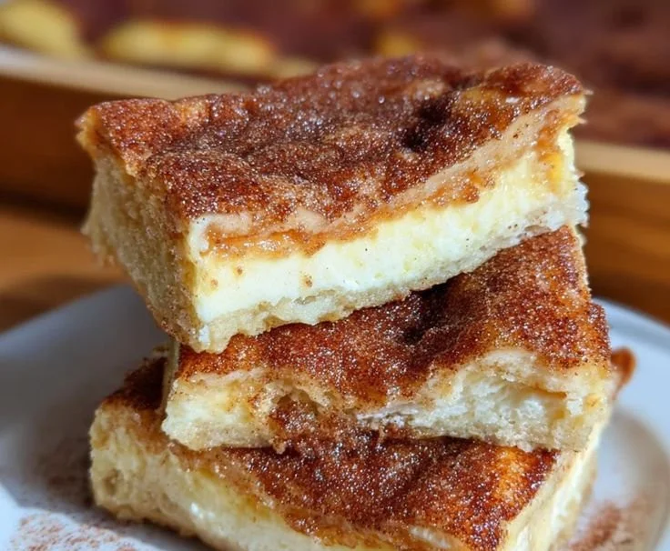 Churro cheesecake bars with cream, cinnamon, and sugar topping on a plate.