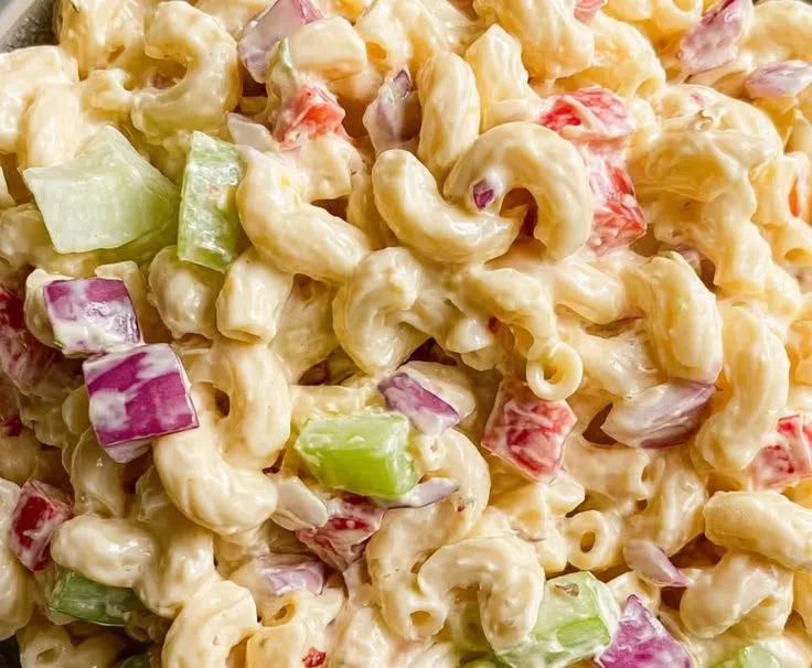 A bowl of classic macaroni salad with vegetables and dressing.